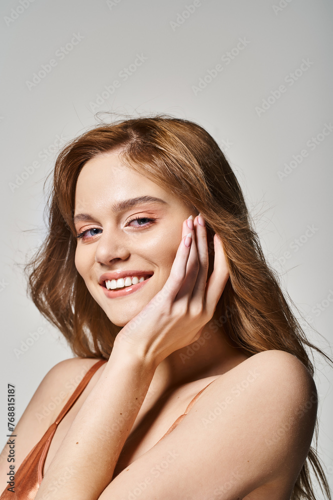 Young pretty woman with perfect skin smiling at camera touching face, on grey studio background Young pretty woman with perfect skin smiling at camera touching face, on grey studio background
