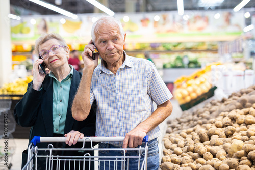 Mature european spouses talking on the phone in supermarket