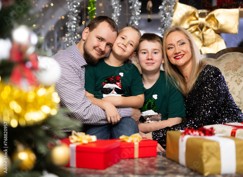 Portrait of happy family with two children celebrating Christmas next to Christmas tree