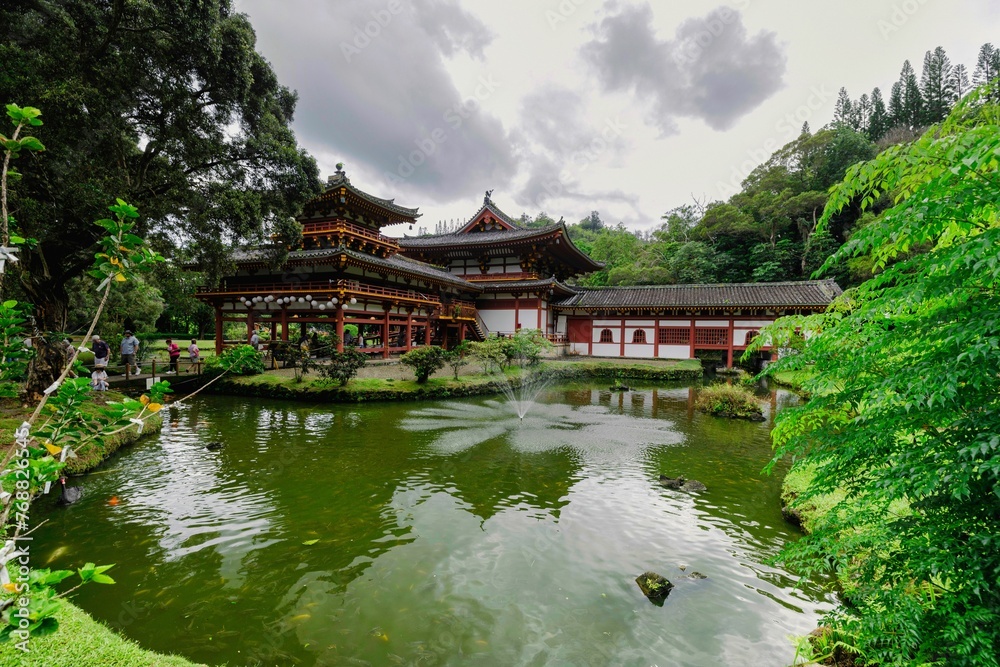 Scenic view of an Asian-style traditional building in a green forest with a pond Scenic view of an Asian-style traditional building in a green forest with a pond