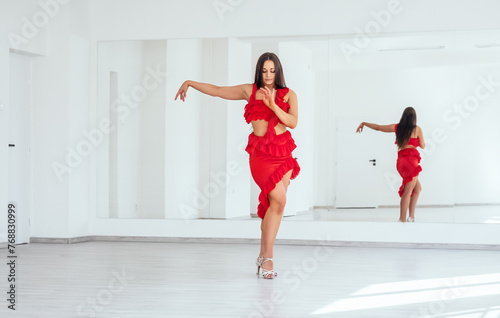 Graceful woman dressed in red Latin dancing dress doing elegant dance movings in white color big hall with big mirror wall. People's expressions during dancing, beauty of woman's body concept image