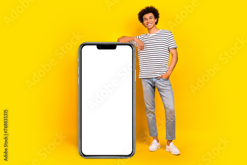 Full body cadre of young satisfied promoter guy xiaomi gadget update for users near board display phone isolated on yellow color background