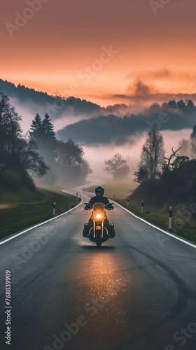 A motorcyclist riding through the countryside on an early spring morning, an empty road with mist over the surrounding fields and valleys, a mystical atmosphere.