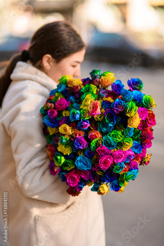 Young woman holds a bunch of bright multi-colored roses without wrapping
