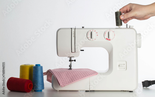 The hand of a seamstress holds a modern automatic sewing machine on a white background with multi-colored spools of thread. Copy space for text. Tailoring services photo