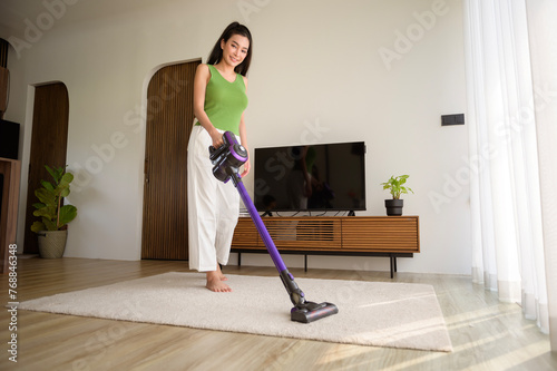 Young happy woman using a vacuum cleaner the floor in living room