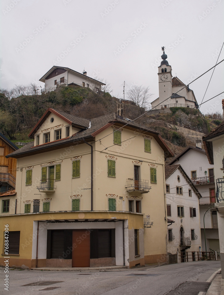 Obraz premium Old residential buildings in the mountain village of Rigolato in Carnia, Friuli-Venezia Giulia, North East Italy. The Parish Church of Saints Philip and James is in the background, Chiesa Parrocchial