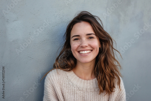Portrait of a young woman with a bright smile standing confidently in front of a monochromatic grey wall