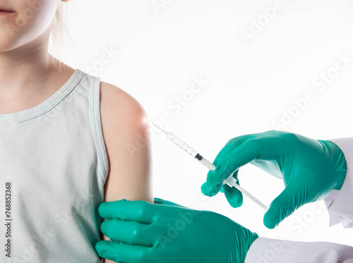 The hands of a doctor in green medical gloves make a vaccination against diphtheria, whooping cough and tetanus in the shoulder of a child girl. Copy space for text, revaccination photo