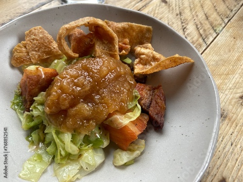 roast pork belly with apple sauce crackling and hispi cabbage on white plate on wood table photo