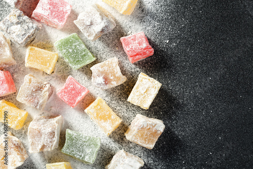 Top down view of a variety of turkish delight candies in different colors and taste, scattered on a black kitchen board, covered with powdered sugar. Colorful food background with copy space