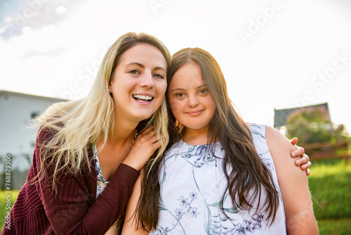 A Portrait of trisomie 21 adult girl smilin outside at sunset with family friend