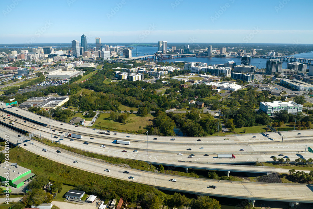 Aerial view of Jacksonville city with high office buildings and american freeway intersection with fast driving cars and trucks. View from above of USA transportation infrastructure