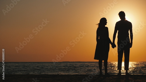 Silhouettes of a young couple in love standing near the sea at sunset