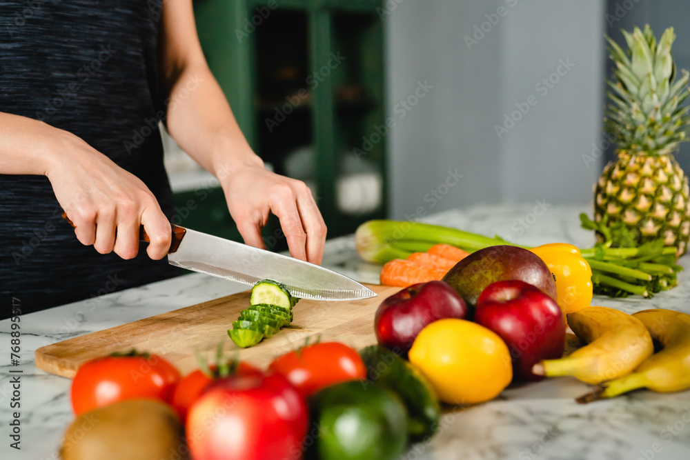 Girl`s hands cutting vegetables on cutting board, close up shot. Healthy eating concept. Colorful variety of fruits and vegetables at home kitchen. Vitamins and fiber source