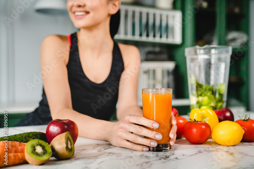 Healthy young girl holding fresh detox smoothie in the kitchen. Orange juice for healthy eating. Slimming and calories losing concept. Vegan and vegetarian meal food