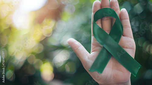 Mental health awareness week background - green ribbon in a hand with bokeh background photo