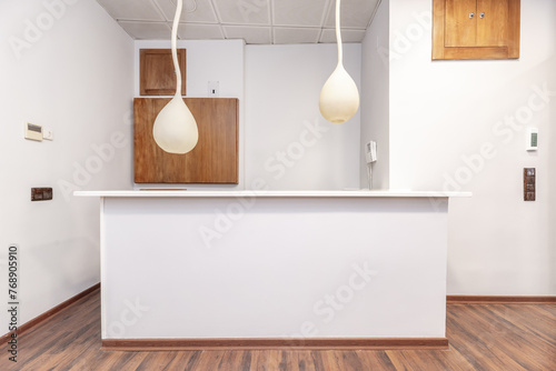 Frontal image of a white reception desk and some hanging lamps above the counter