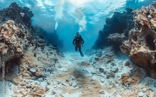 Diver hovers over the sandy sea floor flanked by rocky cavern walls that stretch