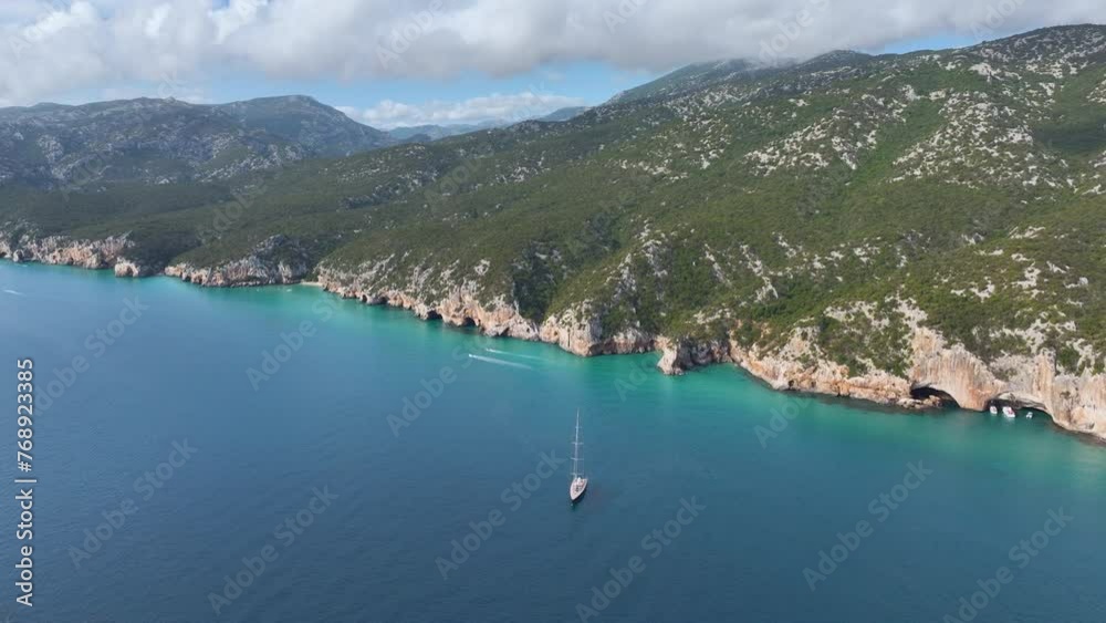 Aerial shot - Sardinian mountain range, view from the rocky coastline with one lonely sail boat in the sea. Aerial shot - Sardinian mountain range, view from the rocky coastline with one lonely sail boat in the sea.