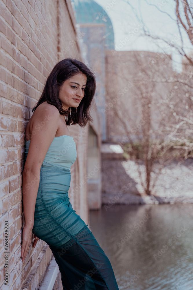 A woman in a green and white dress leans against a brick wall A woman in a green and white dress leans against a brick wall