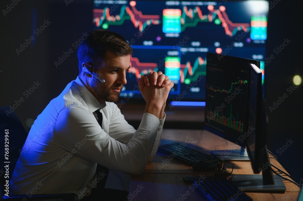 Side view of crypto broker sitting at office table, analyzing market, looking at screen Side view of crypto broker sitting at office table, analyzing market, looking at screen