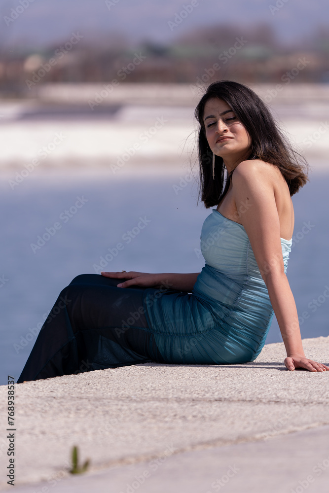 A woman in a blue dress is sitting on a ledge by a body of water