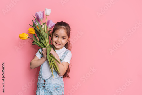 Child holding a bouquet of tulips in front of a pink background. photo
