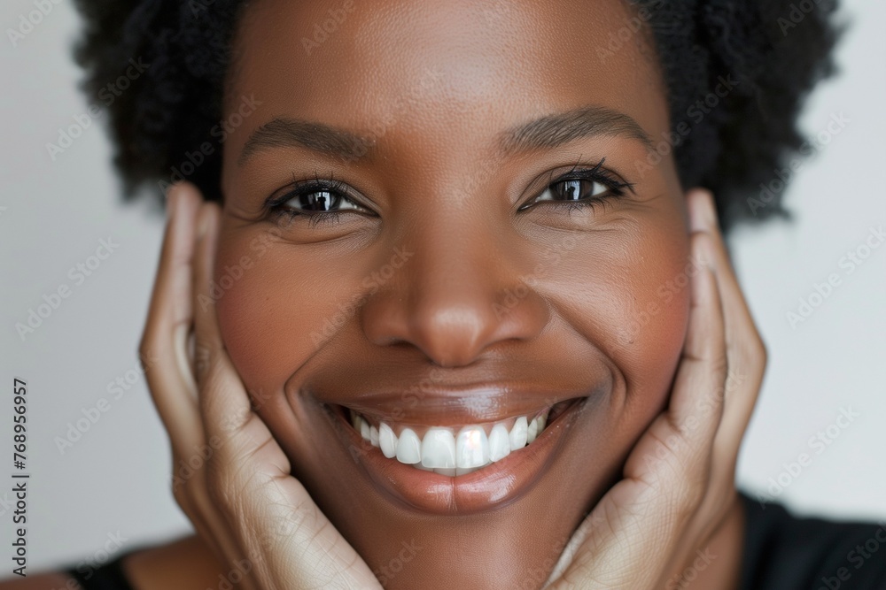 woman laughing with her hands, her head tilted back and eyes closed in joy. She has short hair styled. The background is neutral with soft lighting, highlighting her expression and skin texture.