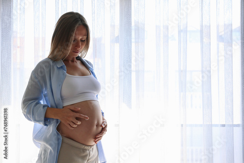 Young pregnant woman standing by the window, applying anti stretch mark cream to her belly. Close up, copy space, background. Free Download Young pregnant woman standing by the window, applying anti stretch mark cream to her belly. Close up, copy space, background. - GFXLoad