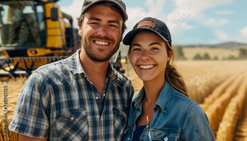 Happy young adult couple farmers, portrait in the wheat field in front of combine harvester.