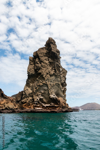 pinaculo de roca volcánica con volcán de fondo en bahía de agua turquesa en Galápagos