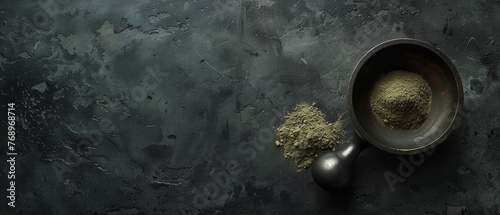   A bowl of green powder sits on a black surface next to two spoons The background is dark gray