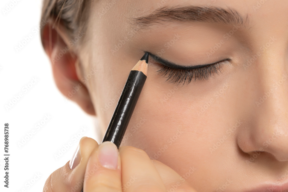 woman applying eyeliner on eyelid with pencil on a white background