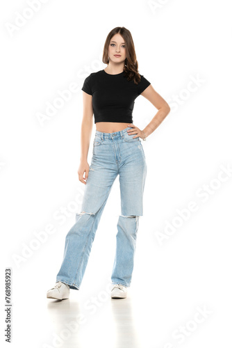 Young female model wearing ripped jeans and black shirt posing on a white background. Front view