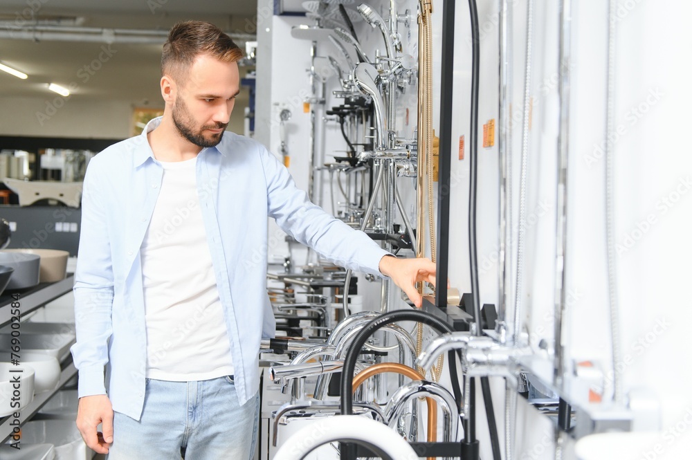 A large selection of water faucets. Man chooses a products in a sanitary ware store A large selection of water faucets. Man chooses a products in a sanitary ware store