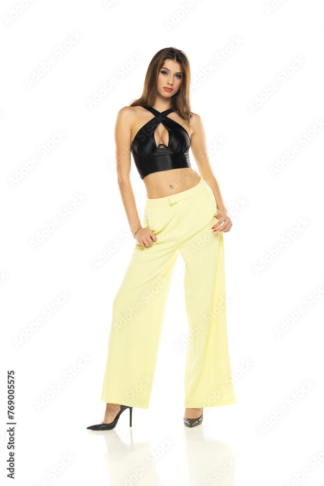 Fashion model posing in black blouse, yellow loose pants and high heel shoes on a white background