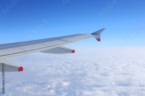 Plane wing flying above the clouds and blue sky.