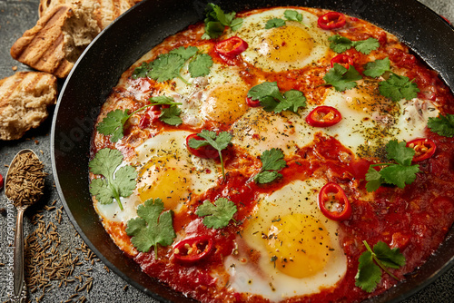 Tasty Shakshuka eggs in a pan with toast on a dark concrete background. Eggs poached  in a spicy tomato pepper sauce. Traditional Jewish scrambled eggs.
