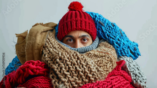 A person is enveloped in an array of chunky, colorful knitted scarves and wearing a red beanie.
