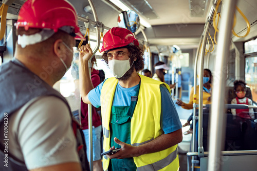 Construction workers with safety helmets and face masks talking on public bus photo