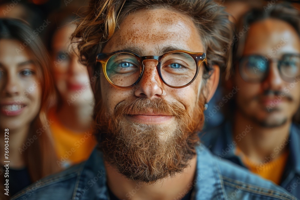 Close-up of a bearded man with glasses smiling confidently among other individuals Close-up of a bearded man with glasses smiling confidently among other individuals