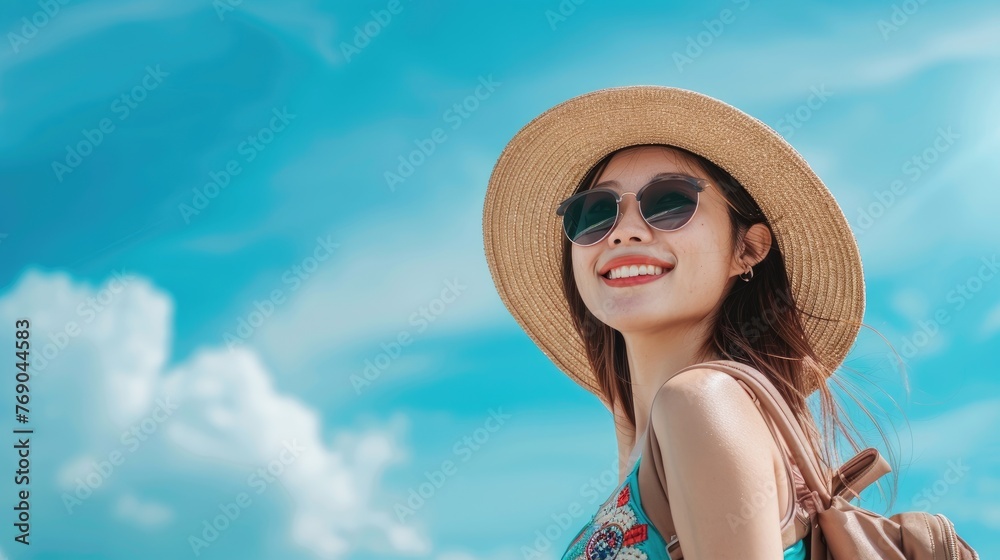Close-up Beautiful Happy young Asian tourist woman wearing a beach hat, sunglasses, and backpacks going to travel on holidays on a blue sky background. travel concept.
