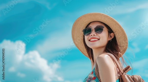 Close-up Beautiful Happy young Asian tourist woman wearing a beach hat, sunglasses, and backpacks going to travel on holidays on a blue sky background. travel concept.