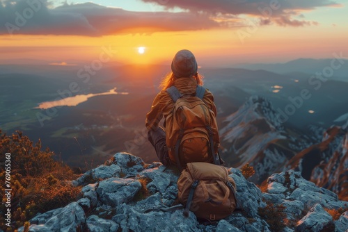 A solitary hiker with a backpack stands atop a mountain, taking in the vast sunset panorama before her photo