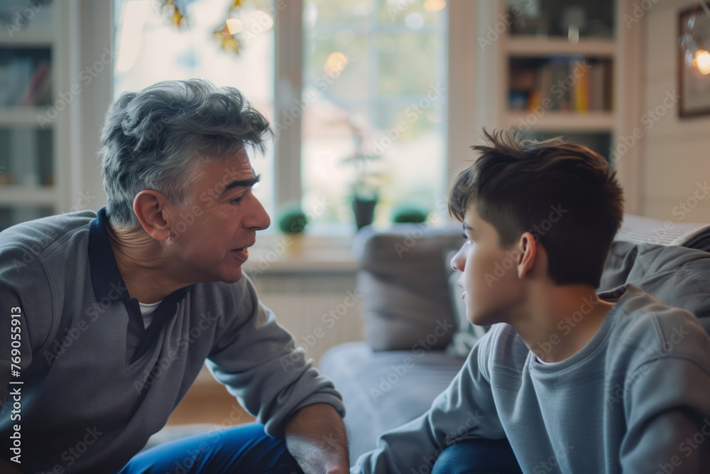 Father and teenage son having conversation in sunny living room. Bonding, communication and relationship concept.