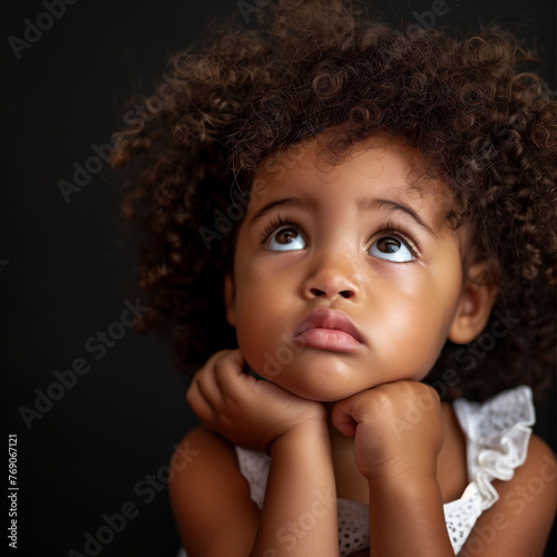 A pensive isolated black child rests their chin on hands, eyes wide with wonder, epitomizing a moment of childhood curiosity and introspection, African American girls portrait..