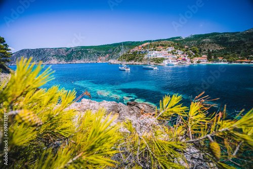 Amazing Assos village, Kefalonia. Greece. White cruise yachts staying at anchor in beautiful emerald green colored lagoon water. Framed by pine trees branches