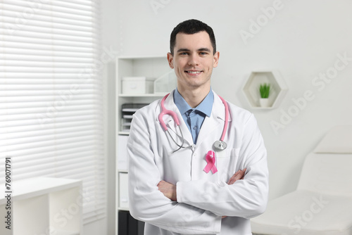 Portrait of smiling mammologist with pink ribbon and stethoscope in hospital. Breast cancer awareness