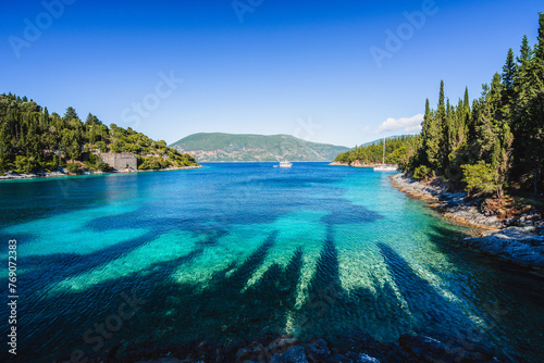 Beautiful Phoki Beach surrounded by cypress trees in the evening sunlight. Amazing seascape of Ionian Sea. Cypress shadows on the clear azure water. Greece